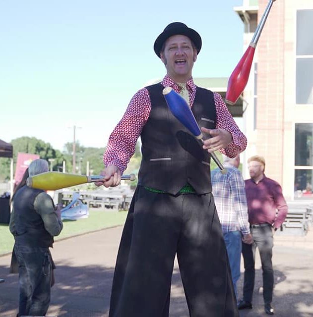 Tom juggling clubs on stilts